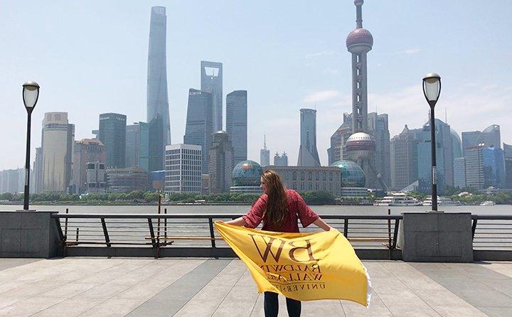 Business major Gwyn Dubel in China holding a Baldwin Wallace flag in front of a skyline.